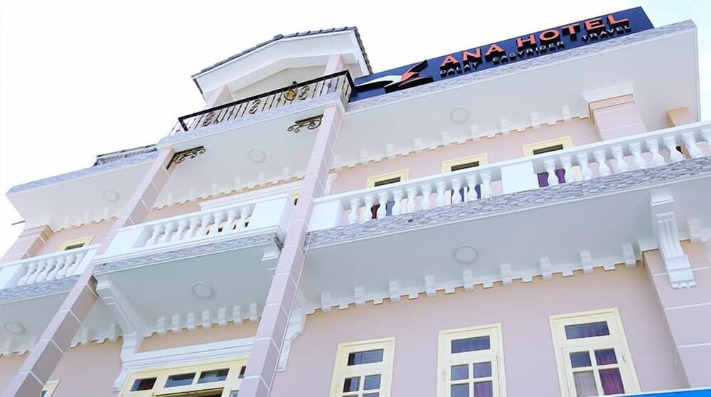 A charming pink hotel with white balconies and a bold "ANA HOTEL" sign offers travelers a cozy and inviting accommodation option in an urban setting.