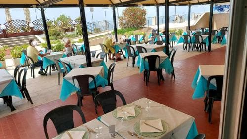 A vibrant outdoor dining area with tables set under a canopy, featuring turquoise tablecloths and a relaxed seaside ambiance, perfect for travelers seeking a leisurely meal by the beach.