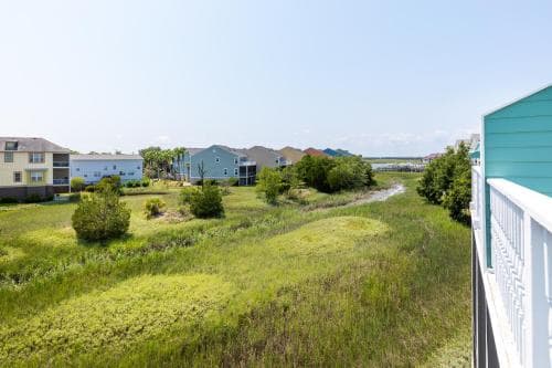 A serene coastal view from a balcony showcases lush greenery, scattered houses, and a clear sky, ideal for relaxing getaways and nature lovers seeking tranquility.
