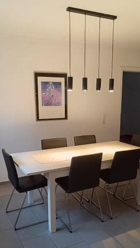 A modern dining room features a sleek white table surrounded by black chairs under stylish pendant lights, creating an inviting atmosphere ideal for travelers seeking contemporary accommodations.