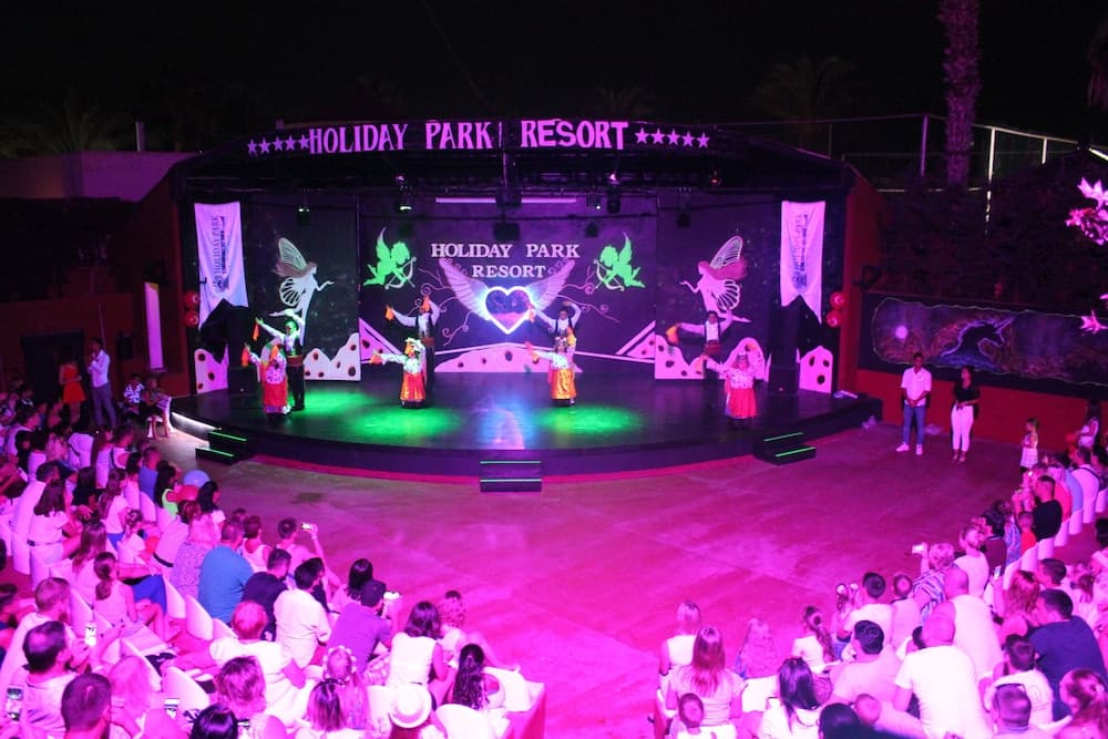 A vibrant evening performance at a resort stage, illuminated by colorful lights and surrounded by an engaged audience, creates a festive atmosphere perfect for family entertainment and vacation memories.