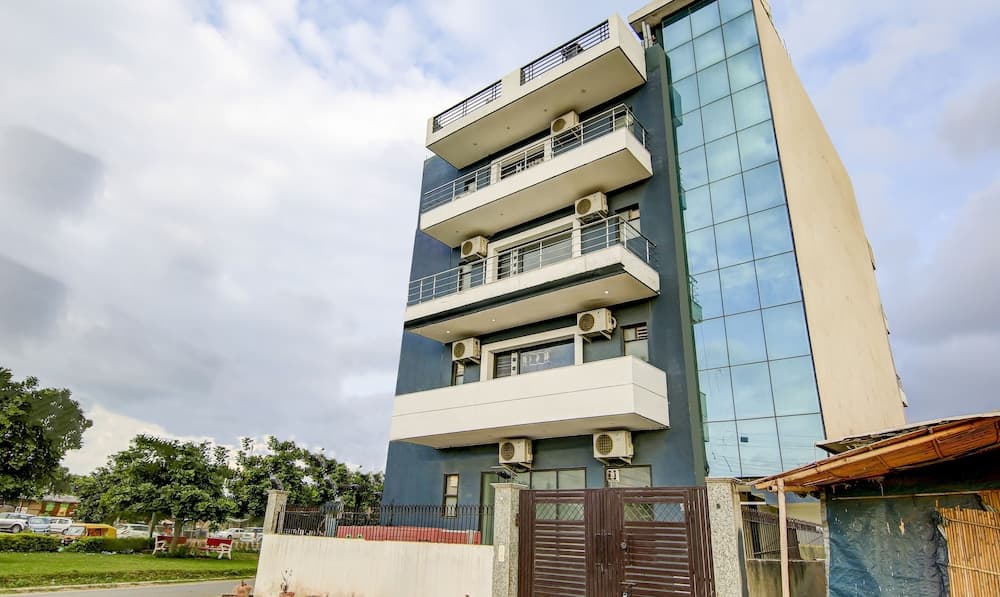 A modern multi-story building with glass panels and balconies stands under a partly cloudy sky, surrounded by greenery, ideal for business travelers seeking professional accommodations.