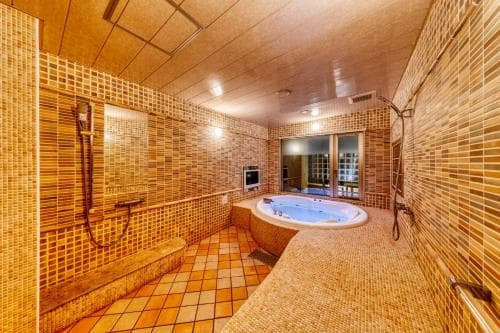 A cozy spa room with warm-toned tiled walls features a central jacuzzi tub, benches, and a serene ambiance, ideal for relaxation and wellness retreats.