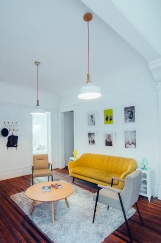 A cozy living room with a vibrant yellow sofa, wooden floors, and minimalist decor creates an inviting atmosphere, perfect for travelers seeking a stylish and comfortable rental space.