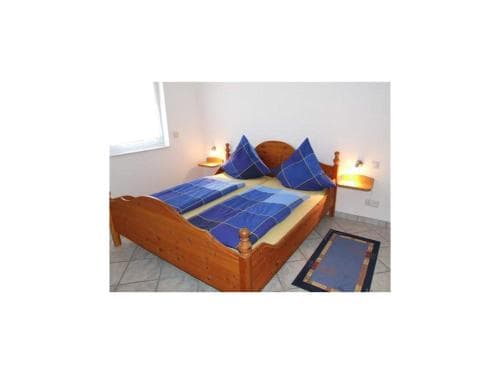 A cozy bedroom with a wooden bed adorned in blue bedding, wall-mounted lamps, and a tiled floor creates a serene atmosphere ideal for travelers seeking a peaceful retreat.