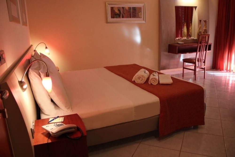 A cozy hotel room with warm lighting, neatly arranged towels on the bed, a desk by the window, and inviting decor, perfect for travelers seeking comfort and relaxation.