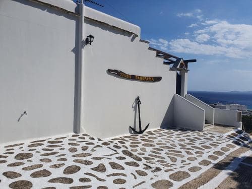A serene coastal scene features a white-washed building with an anchor decoration on a cobblestone path, ideal for travelers seeking picturesque Mediterranean charm.