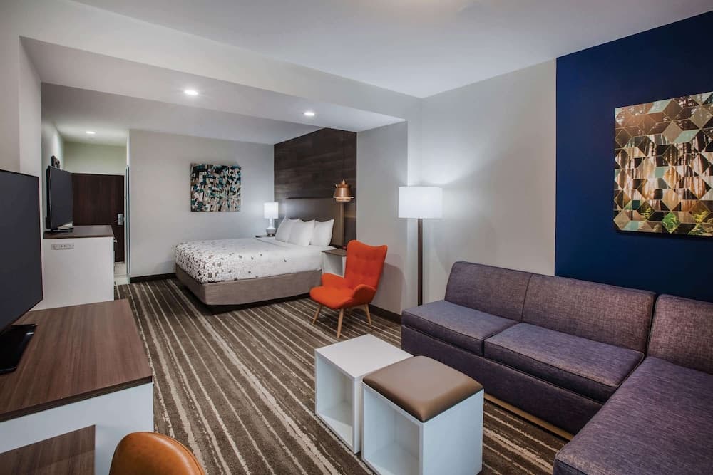 A cozy hotel suite features a modern living area with a purple sofa, orange armchair, and abstract wall art, creating a welcoming atmosphere ideal for travelers seeking comfort and style.