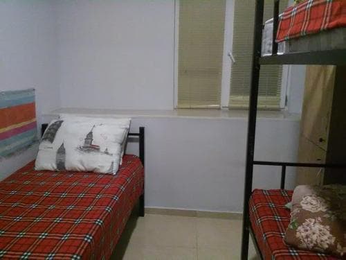 A cozy hostel room with bunk beds adorned in red plaid bedding, featuring a pillow with a cityscape design, set against a minimalist backdrop, ideal for budget travelers seeking a comfortable stay.