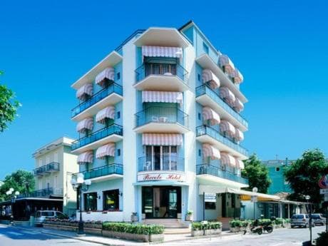 A charming multi-story hotel with striped awnings and balconies stands under a clear blue sky, offering a welcoming atmosphere for travelers seeking a cozy seaside retreat.