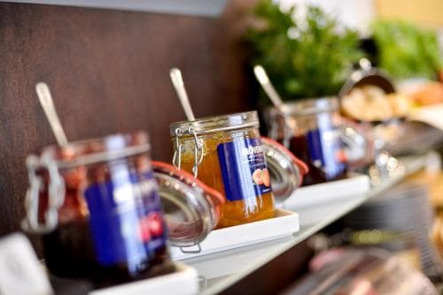 A cozy café buffet scene featuring jars of colorful jams and spreads on a sleek counter, inviting travelers to indulge in a fresh, homemade breakfast experience.
