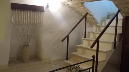 A cozy, warmly lit indoor staircase with rustic wooden railings leads to an inviting upper level, complemented by a decorative vase and soft curtains, perfect for travelers seeking charming accommodations in a historic setting.
