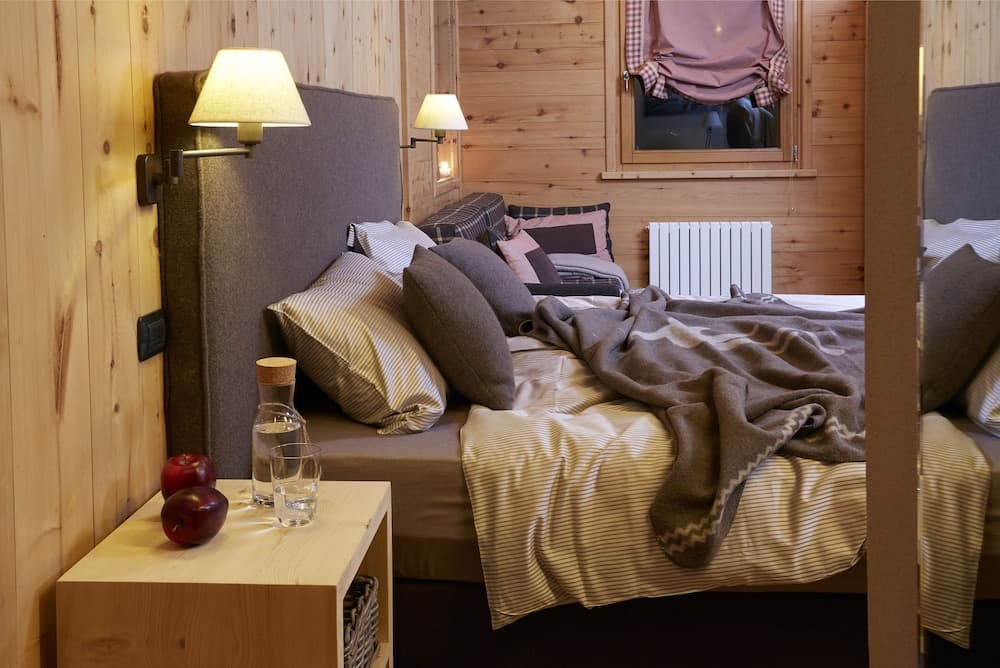A cozy cabin bedroom with wooden walls, soft lighting, and a neatly arranged bed invites travelers seeking a serene retreat, perfect for relaxation and rejuvenation.