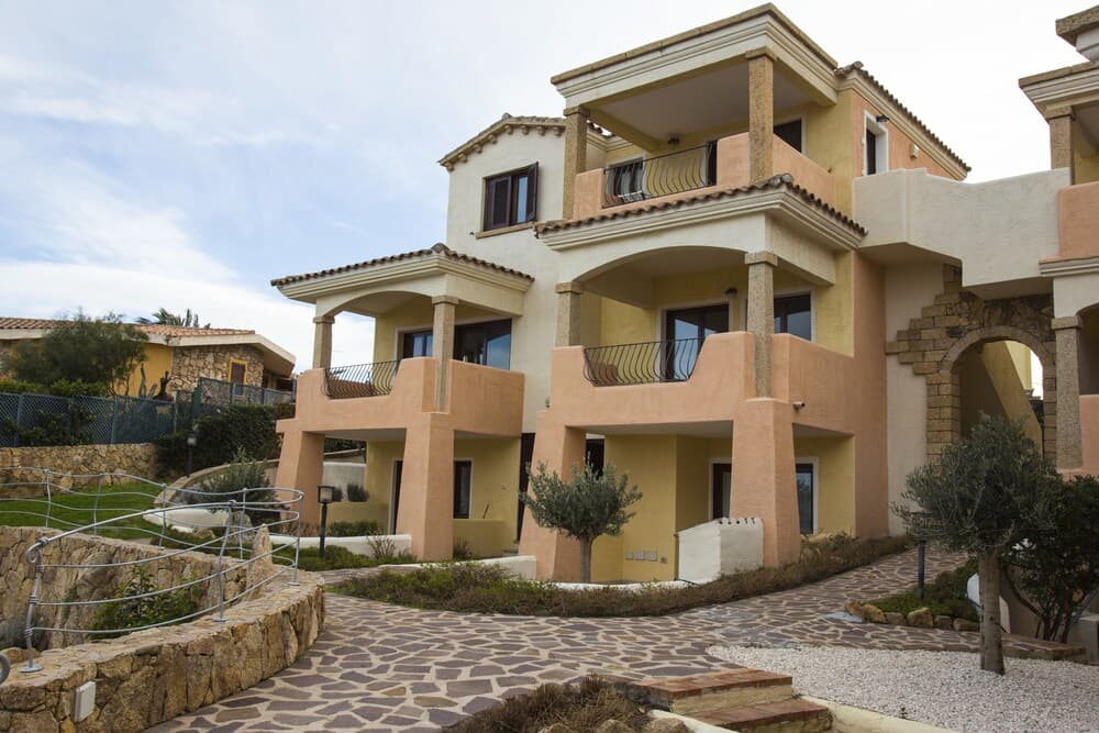 A serene Mediterranean-style villa with terracotta accents, balconies, and lush greenery offers an inviting retreat for travelers seeking luxury accommodations in a tranquil setting.