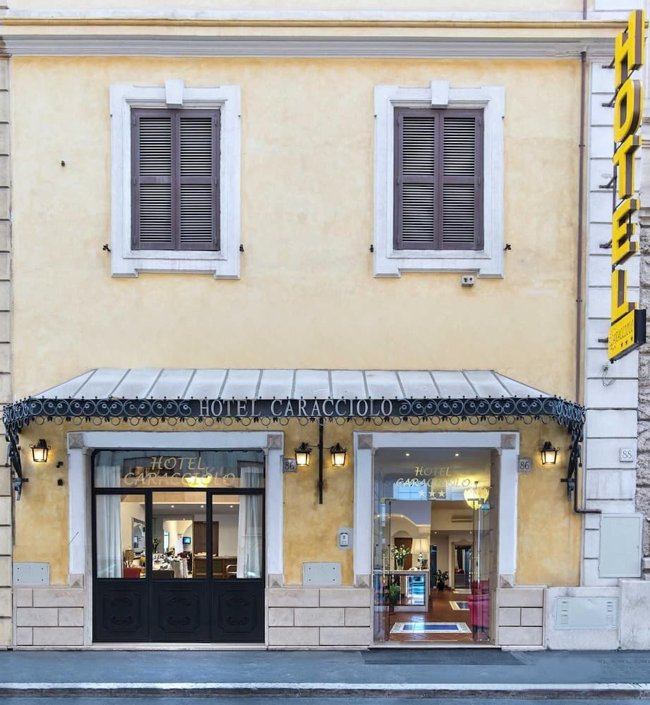 A charming European hotel facade with warm yellow walls, elegant black shutters, and inviting glass doors under a decorative awning, perfect for travelers seeking cozy accommodations in a historic setting.