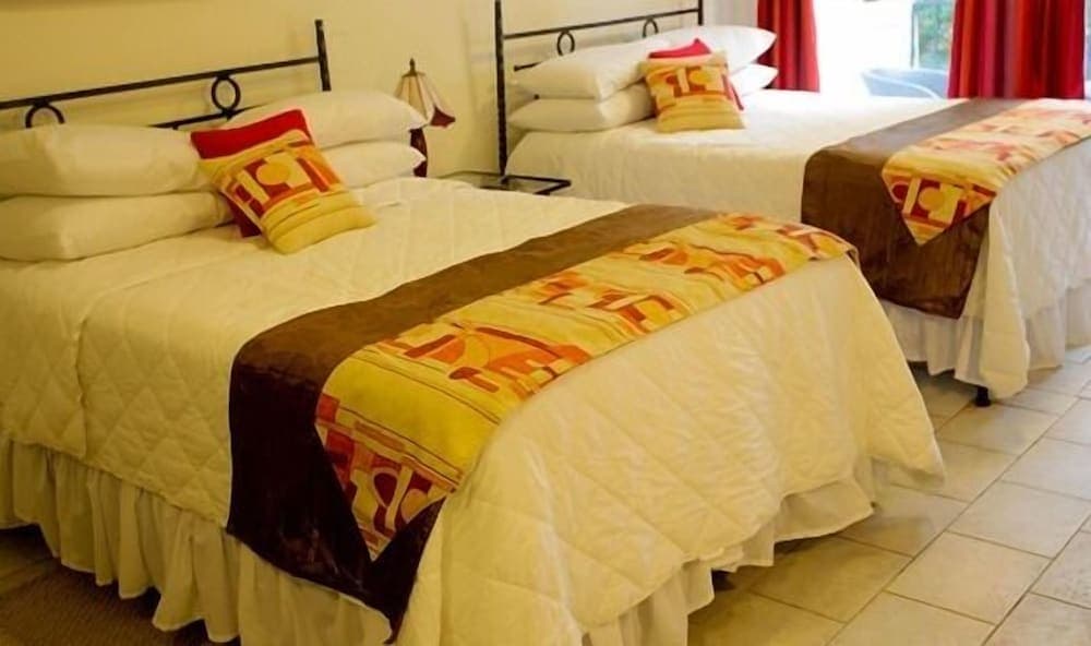 A cozy hotel room features two neatly made beds adorned with vibrant patterned throws and pillows, set against a backdrop of red curtains and tiled flooring, ideal for travelers seeking comfort and relaxation.