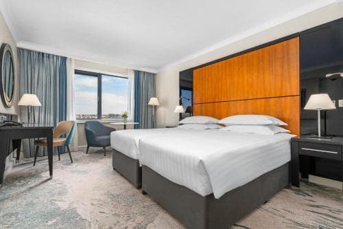 A cozy hotel room with a large bed, wooden headboard, and a scenic view through the window, ideal for travelers seeking comfort and relaxation during their stay.