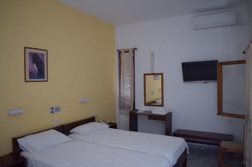 A cozy hotel room with yellow walls, a neatly made bed, wooden furniture, and a mounted TV offers a comfortable stay for travelers seeking simplicity and functionality.