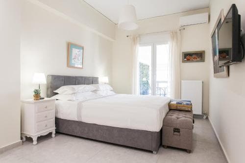 A cozy hotel room features a neatly made bed by a bright window, white furnishings, and a serene atmosphere, ideal for travelers seeking comfort and relaxation.