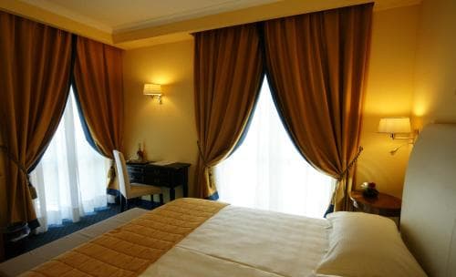A cozy hotel room with warm lighting, plush curtains, and a neatly made bed creates an inviting atmosphere ideal for travelers seeking comfort and relaxation.