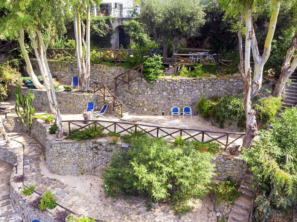 A serene Mediterranean garden with stone terraces, lush greenery, blue lounge chairs, and winding staircases offers a tranquil retreat ideal for relaxation and nature photography.