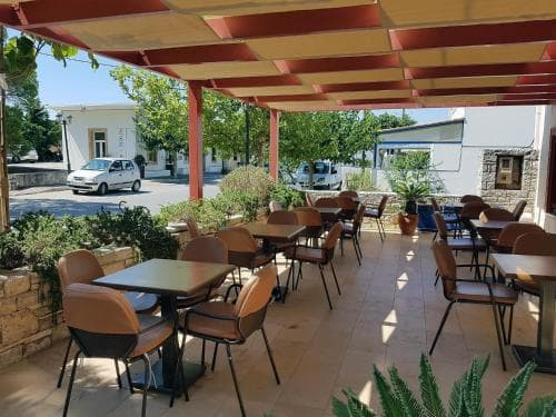 A cozy outdoor café with red-striped awnings, tiled flooring, and greenery offers a relaxed dining spot ideal for travelers seeking a peaceful meal in a sunny Mediterranean setting.
