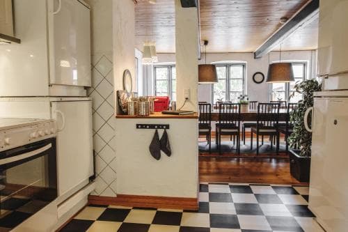 A cozy kitchen with a checkered floor transitions into a warmly lit dining area with wooden accents, ideal for travelers seeking a charming and inviting rental space.