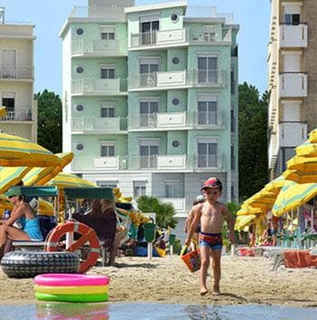 A vibrant beach scene with colorful umbrellas, playful children, and pastel apartment buildings in the background offers a cheerful seaside getaway perfect for family vacations.