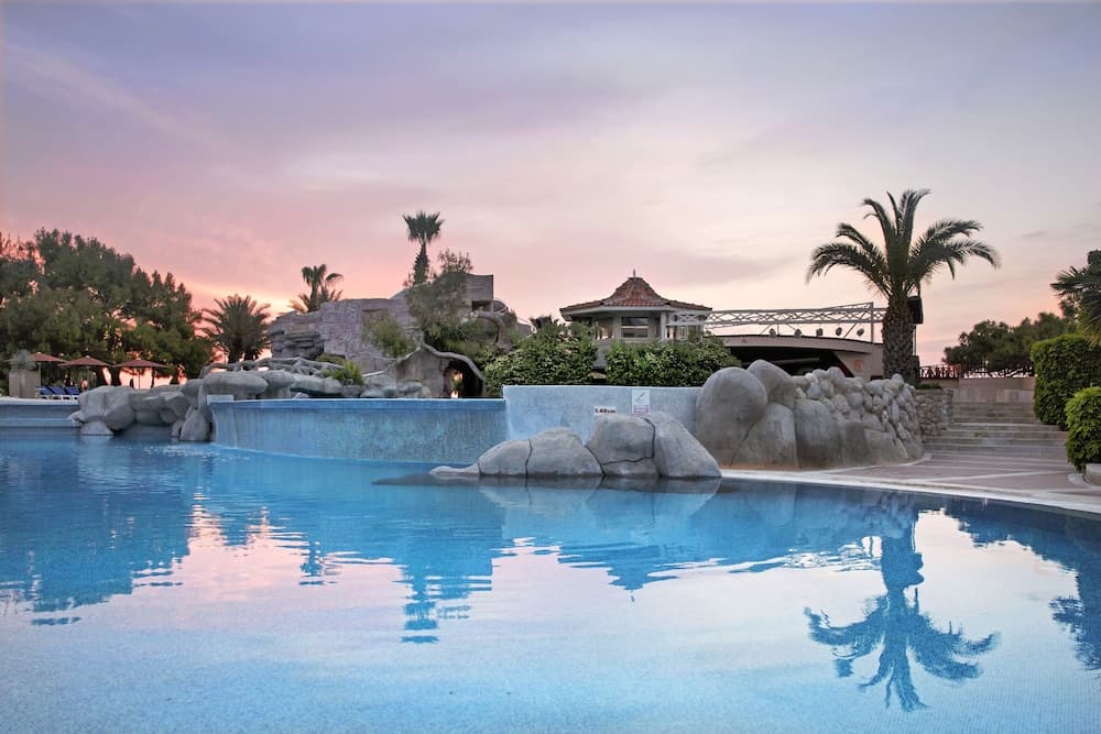 A serene resort pool at dusk reflects palm trees and a tranquil sky, ideal for relaxation and leisure travel photography.