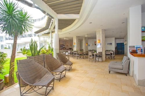 A serene hotel lobby with wicker chairs, lush greenery, and tiled floors offers a relaxing atmosphere ideal for travelers seeking comfort and tranquility during their stay.