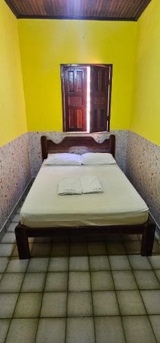 A cozy, minimalist bedroom with vibrant yellow walls, tiled flooring, and a neatly made bed by a wooden door, ideal for budget travelers seeking simple accommodations.