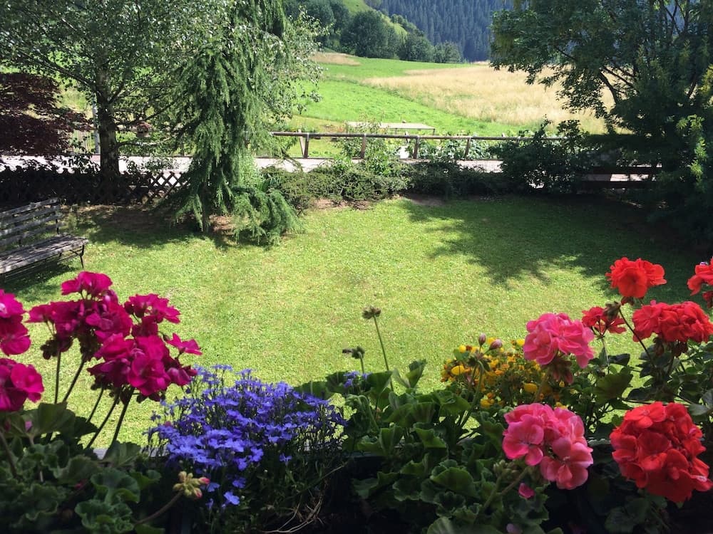 A serene garden view with vibrant flowers in the foreground overlooks a lush green meadow framed by trees, ideal for a relaxing countryside retreat.