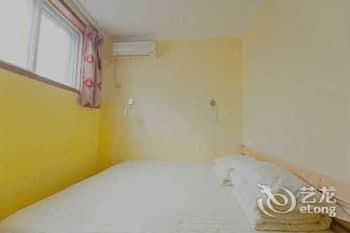 A cozy hotel room with yellow walls, a neatly made bed, and a window with curtains offers a simple and inviting atmosphere for travelers seeking comfortable accommodation.