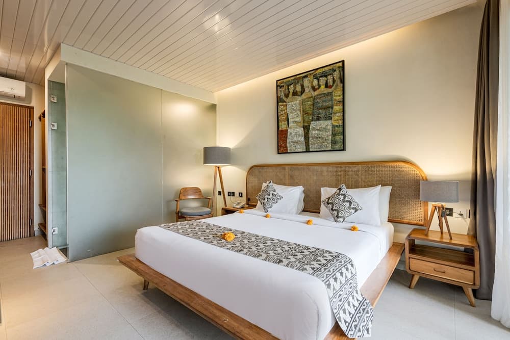 A cozy hotel bedroom features a neatly made bed adorned with patterned linens and yellow flowers, wooden furnishings, and a vibrant wall art piece, creating a serene and inviting atmosphere ideal for travelers seeking relaxation.