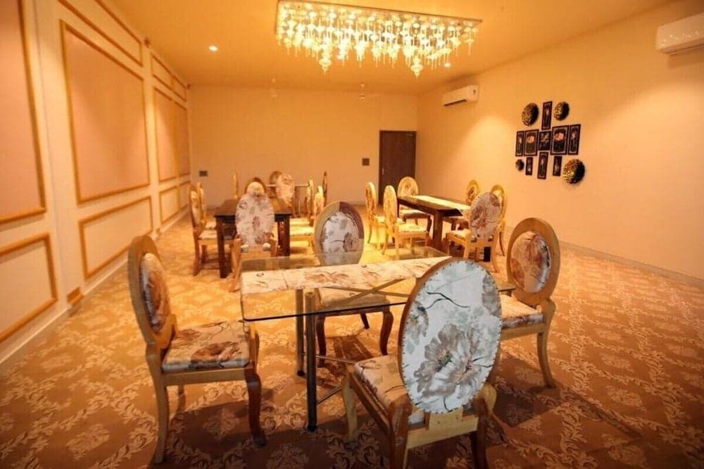 An elegant dining room with ornate floral chairs, glass tables, a sparkling chandelier, and patterned carpet exudes warmth and luxury, ideal for travelers seeking a sophisticated accommodation experience.