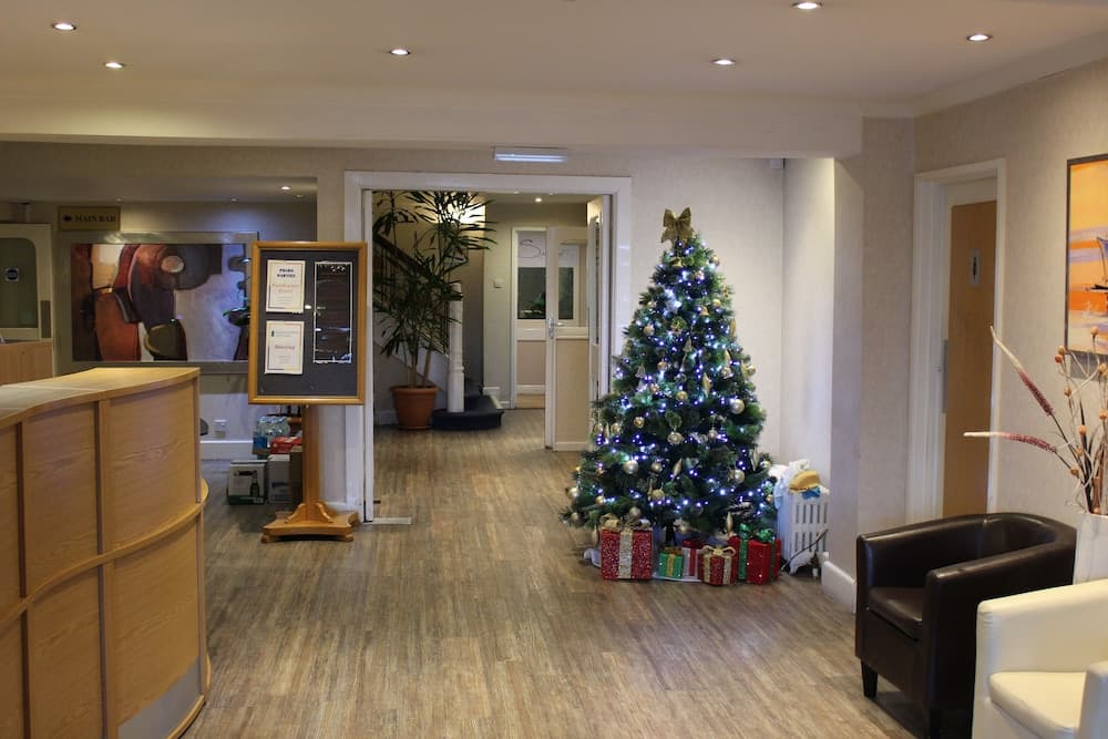 A cozy hotel lobby adorned with a festive Christmas tree surrounded by gifts, featuring modern furnishings, warm lighting, and a welcoming atmosphere ideal for travelers seeking comfort during the holiday season.