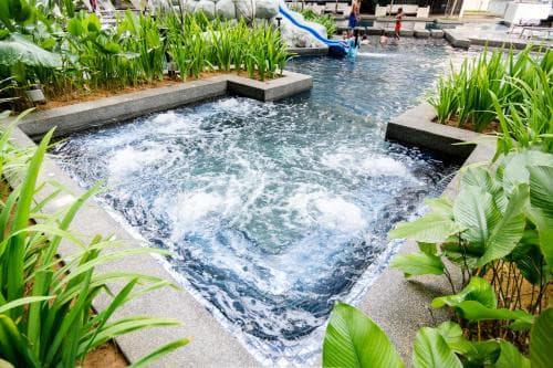 A serene outdoor jacuzzi surrounded by lush greenery offers a relaxing retreat, ideal for travelers seeking rejuvenation in a tranquil spa setting.