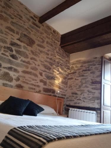 A cozy bedroom with rustic stone walls and wooden beams exudes warmth, featuring a neatly made bed with striped bedding, ideal for travelers seeking a charming countryside retreat.