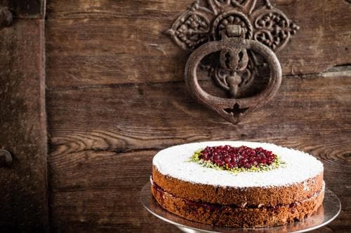 A beautifully frosted cake adorned with cranberries sits elegantly on a rustic wooden backdrop featuring an ornate metal door knocker, perfect for culinary enthusiasts exploring traditional settings.