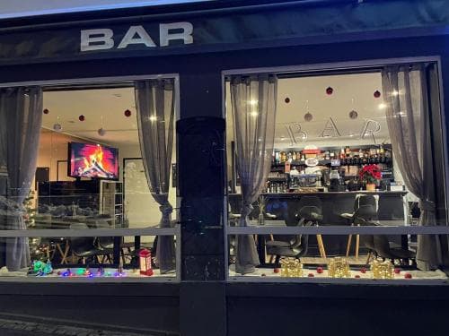 A cozy urban bar illuminated at night with festive decorations, inviting travelers to enjoy drinks and socialize in its warm, welcoming atmosphere.