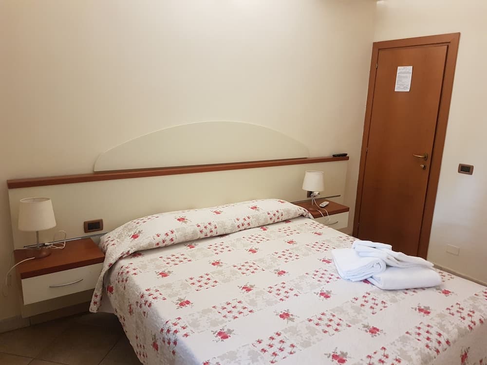 A cozy hotel room features a neatly made bed with floral bedding, wooden bedside tables with lamps, and a warm, inviting atmosphere ideal for travelers seeking comfort and simplicity.