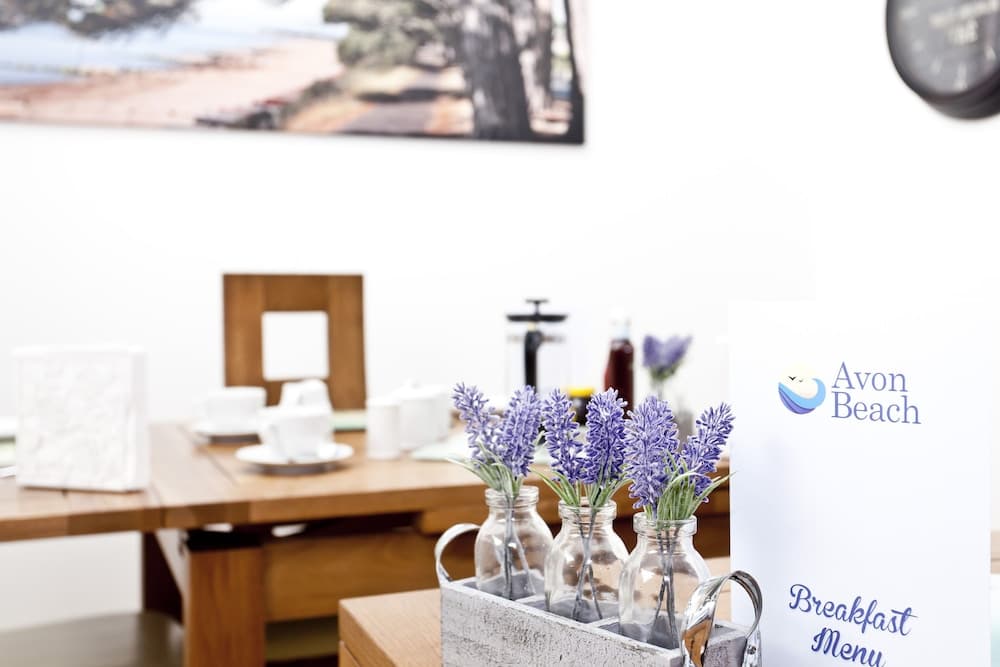 A cozy café setting features lavender flowers in glass jars on a wooden table, complemented by a serene beach-themed artwork, ideal for travelers seeking a relaxing breakfast spot.