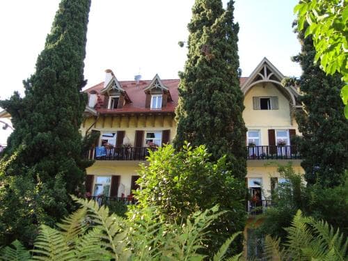 A charming, sunlit villa surrounded by lush greenery and towering cypress trees offers a serene retreat ideal for travelers seeking a peaceful countryside escape.
