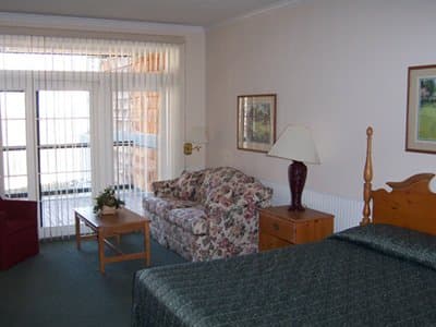 A cozy hotel room features a neatly made bed, floral-patterned sofa, wooden furnishings, and a balcony view, creating a welcoming atmosphere ideal for travelers seeking comfort and relaxation.