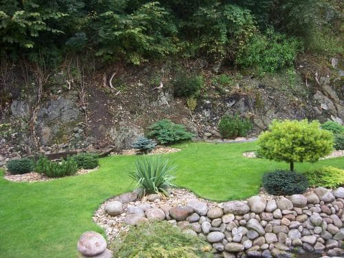 A serene garden with lush greenery, neatly trimmed shrubs, and a rocky stream creates a tranquil atmosphere ideal for relaxation and nature photography.