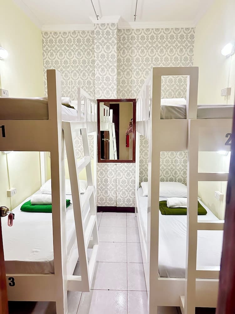 A cozy hostel room with neatly arranged bunk beds, patterned wallpaper, and a mirror reflects a clean and inviting atmosphere, ideal for budget travelers seeking comfortable accommodations.