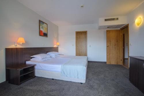 A cozy hotel room features a neatly made bed, wooden furnishings, and soft lighting, creating a welcoming atmosphere ideal for travelers seeking comfort and relaxation.