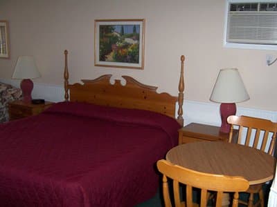A cozy motel room features a neatly made bed with a burgundy comforter, wooden furniture, and a small dining table, creating a welcoming atmosphere ideal for travelers seeking a comfortable stay.