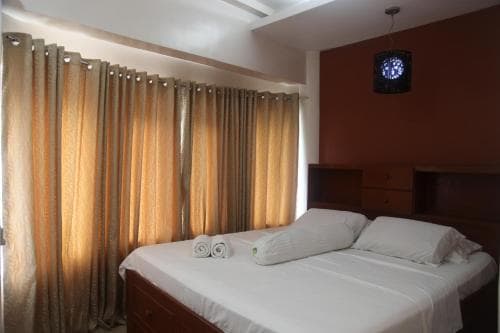 A cozy hotel room features a neatly made bed beside golden curtains, a wooden dresser, and a starry nightlight, ideal for travelers seeking comfort and relaxation.