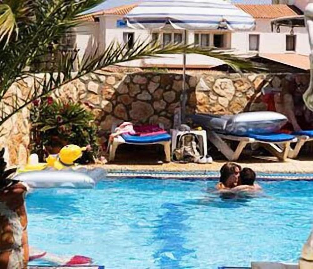 A serene resort pool scene features palm trees, lounge chairs, and a couple embracing in the water under a sunny sky, ideal for vacation inspiration and relaxation-focused travel searches.